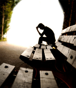 backlit picture of a man sitting on a bench with his hand on his head, only seeing the outline of his body