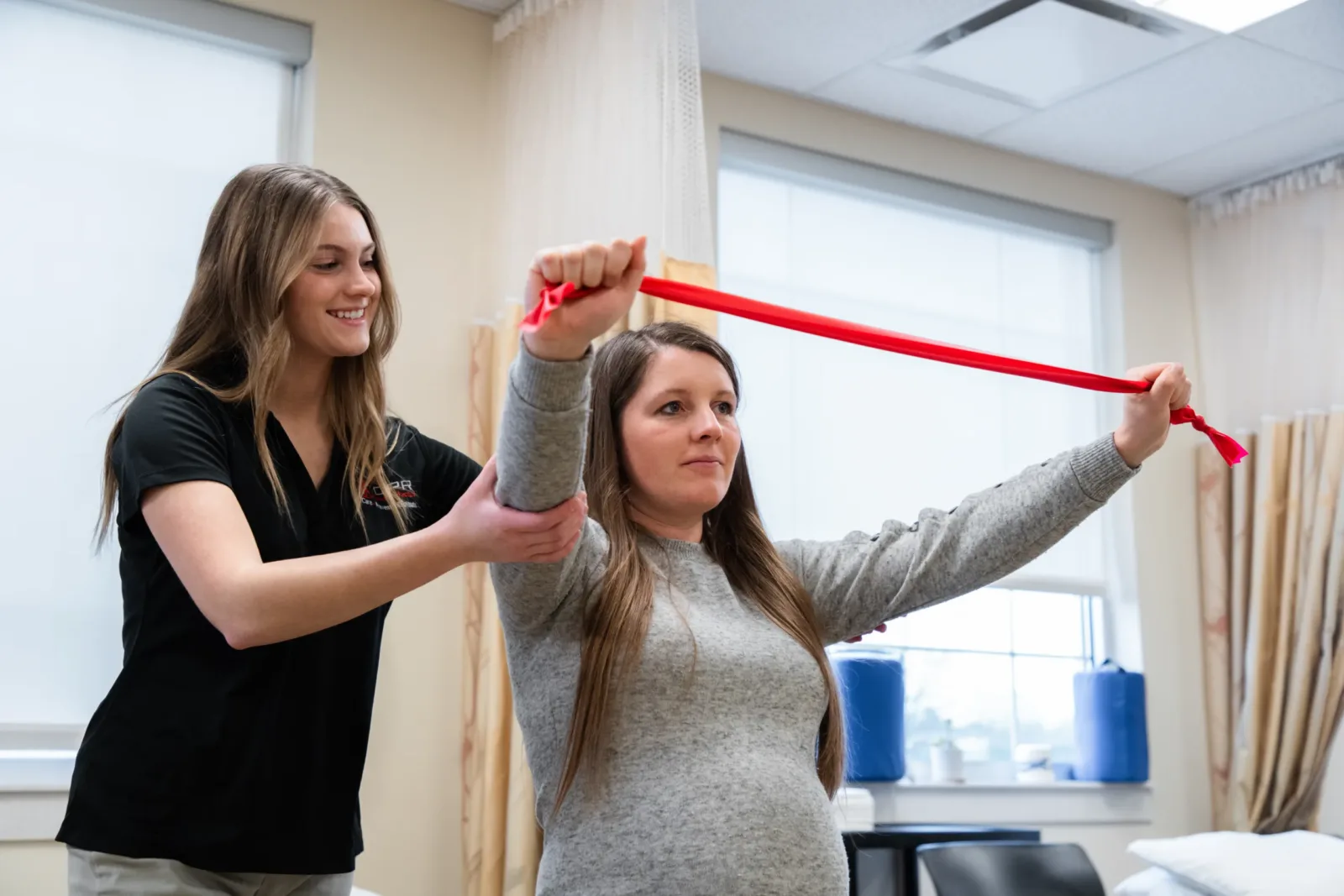 physical therapist helping a pregnant patient use exercise bands