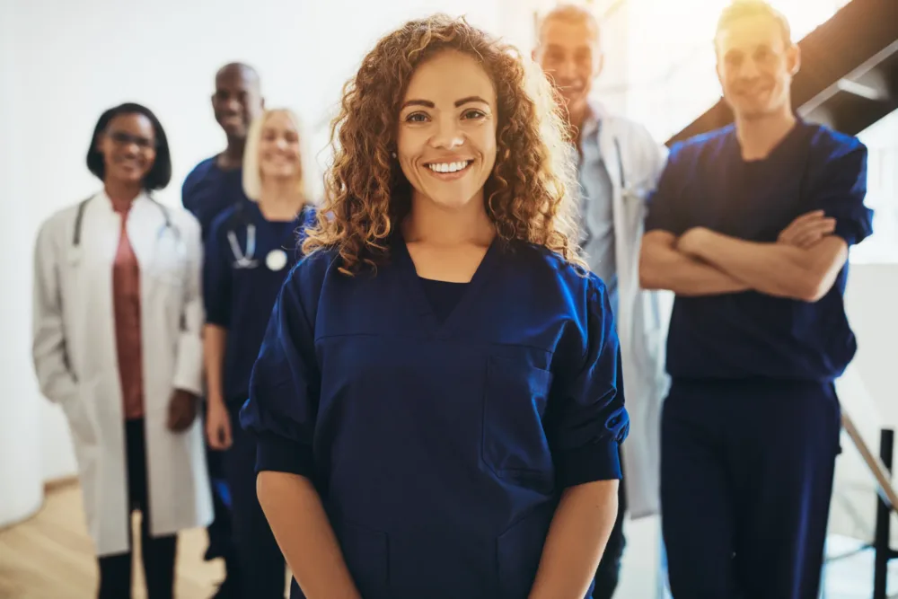 Smiling young female doctor standing in a hospital corridor with a diverse group of medical staff standing behind her